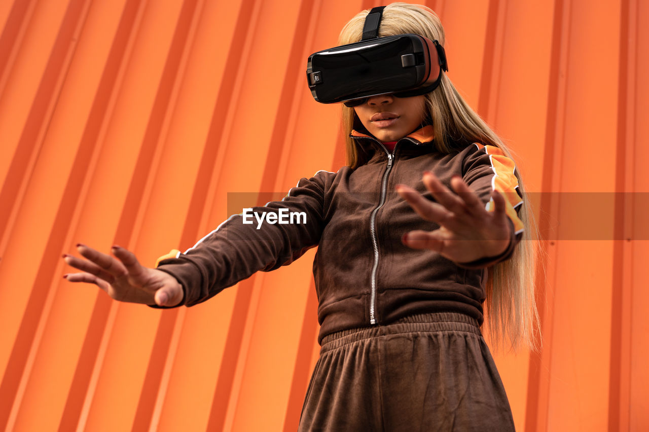 Pretty african american woman using virtual reality glasses on an orange background