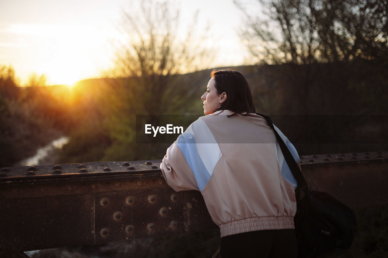 Woman looking at view while standing on bridge after workout during sunset