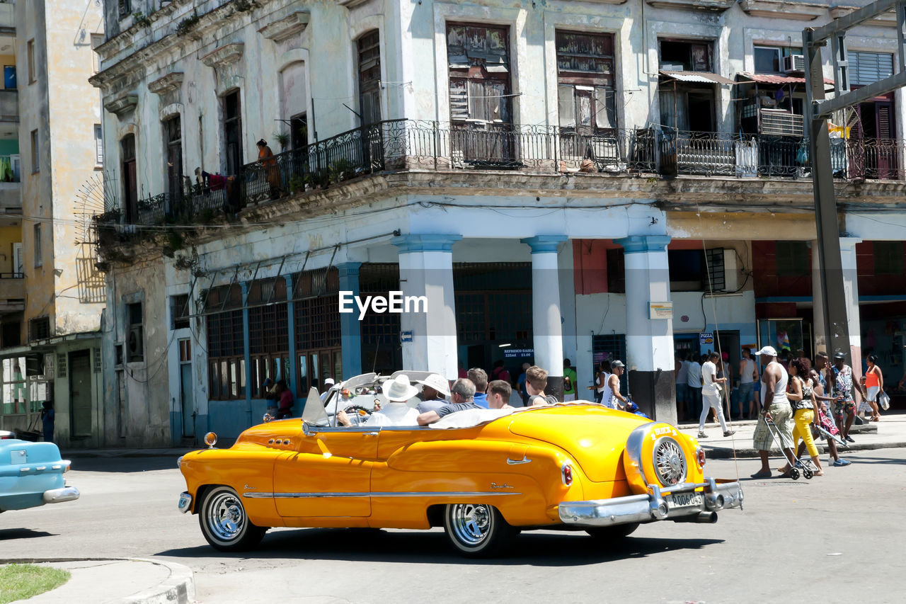 People sitting in yellow car on road against building