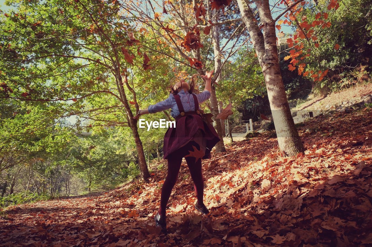 Girl throwing autumn leaves in forest