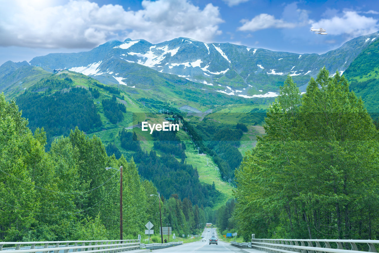 Road amidst trees and mountains against sky