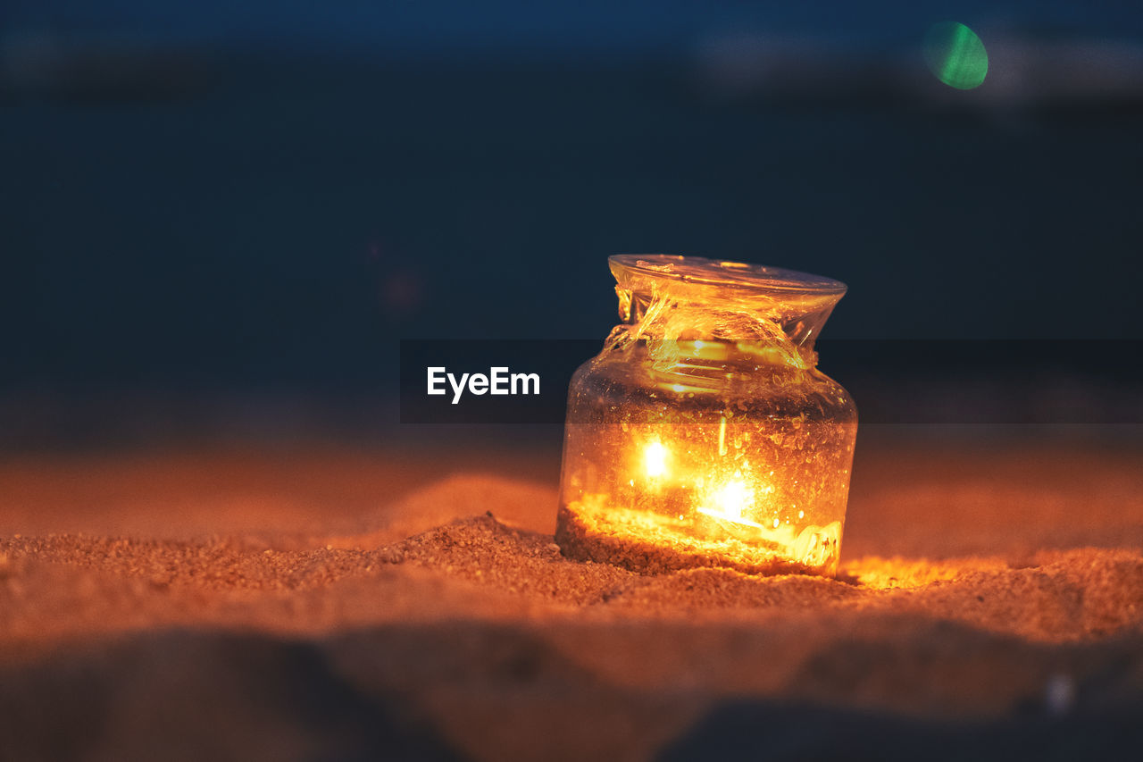 Close-up of illuminated glass jar on sand at night