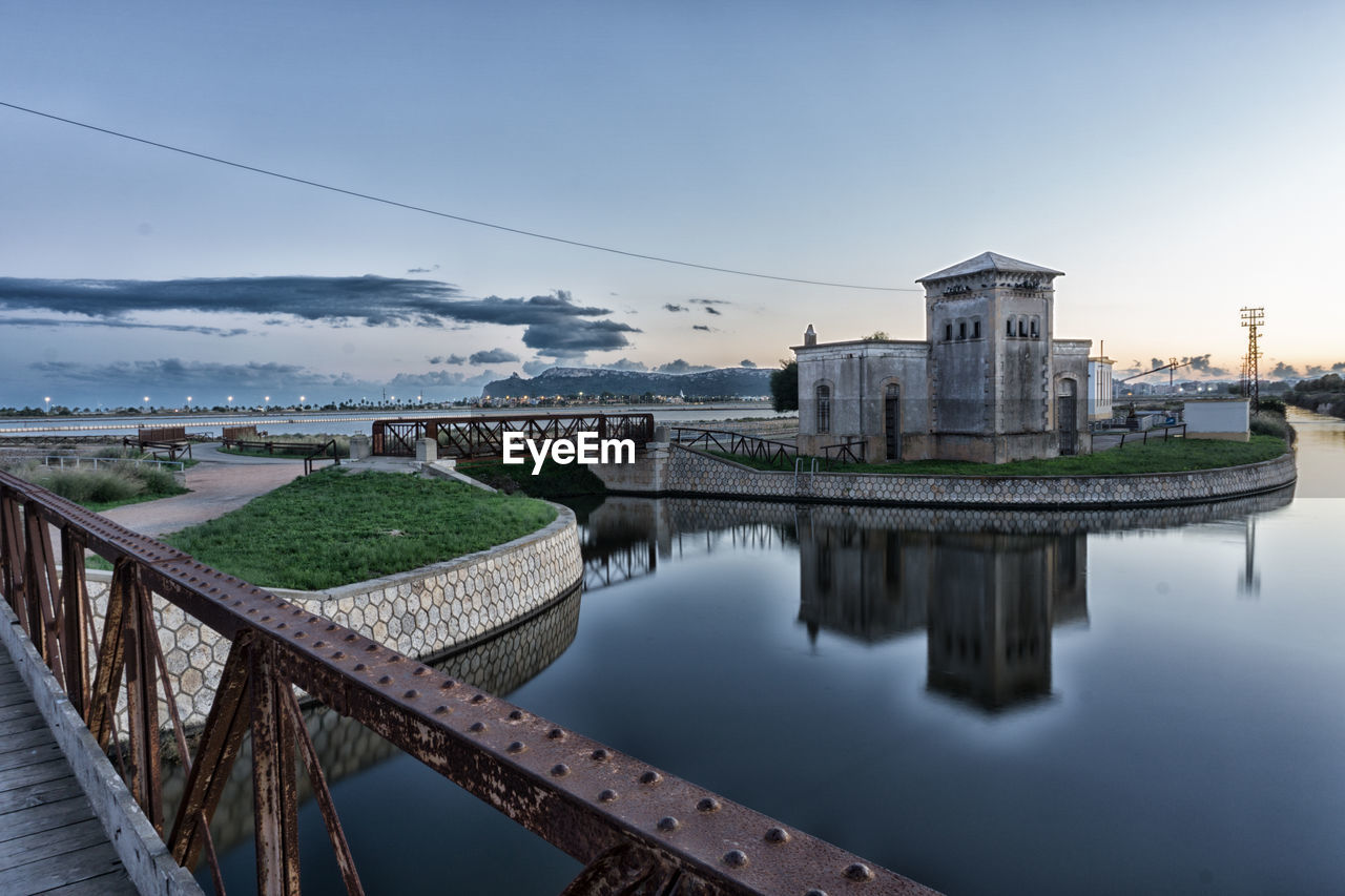 Bridge over river by buildings against sky