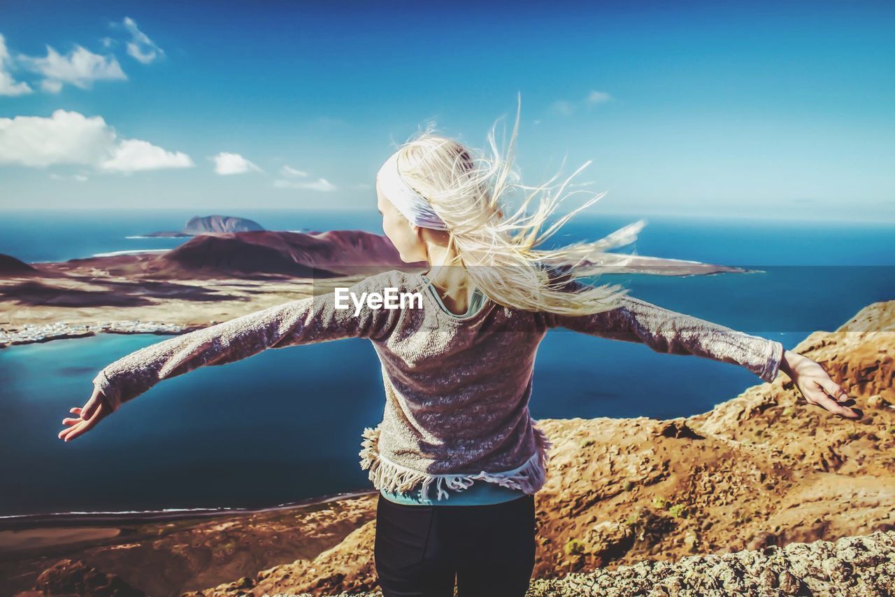 Rear view of woman with arms outstretched by sea against sky