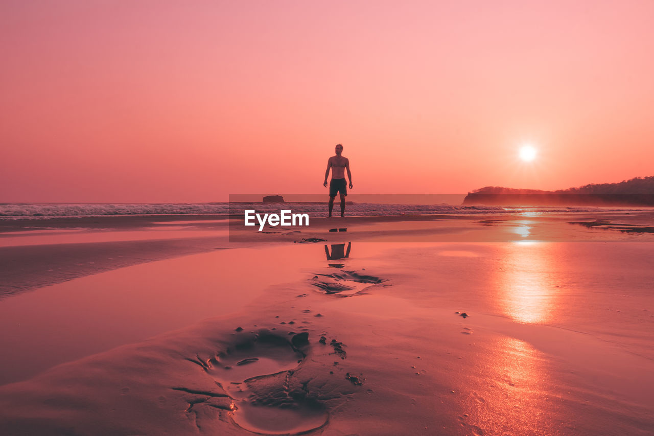 Man on beach against sky during sunset