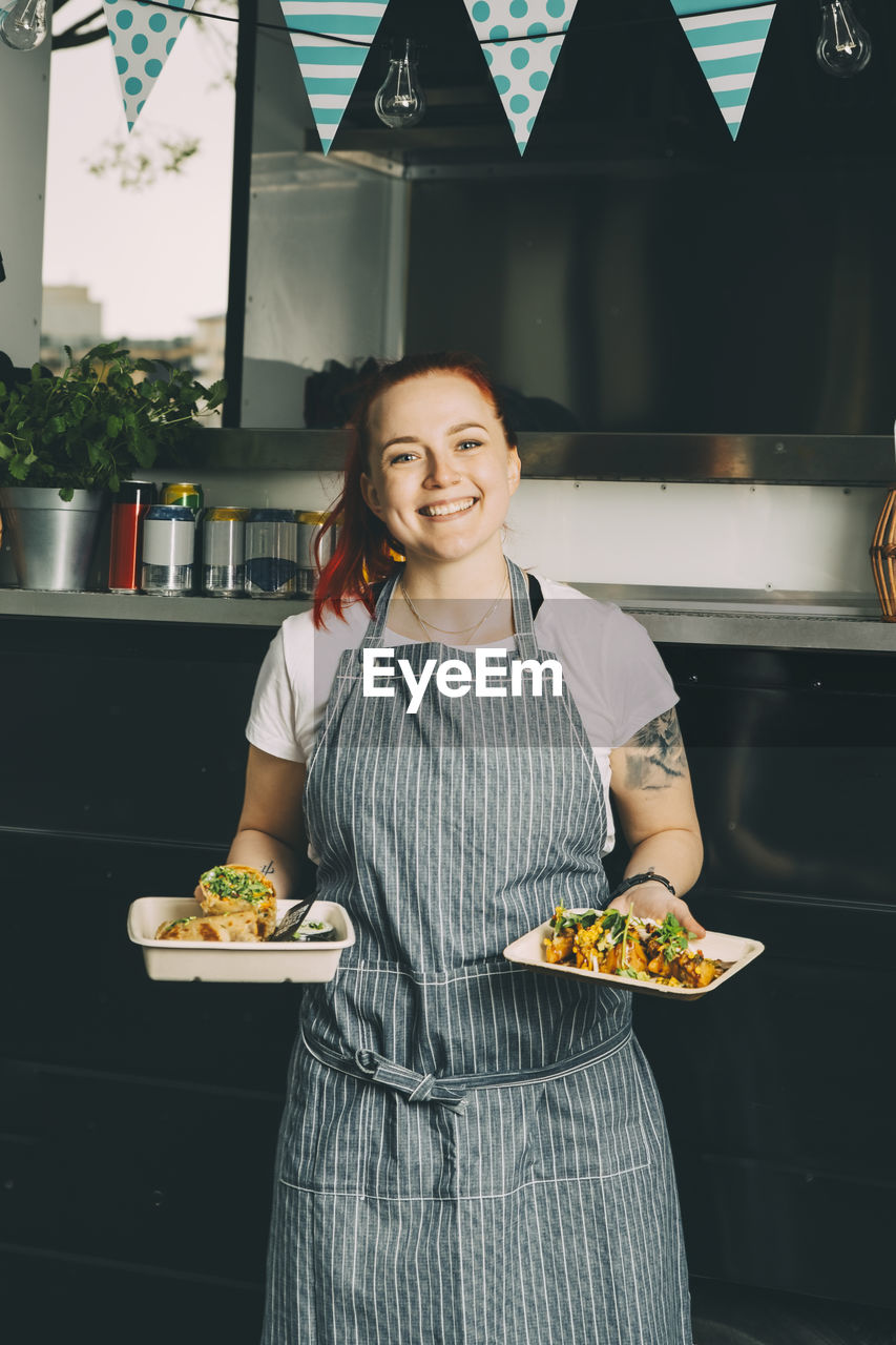 Portrait of smiling owner holding indian food plate against commercial land vehicle