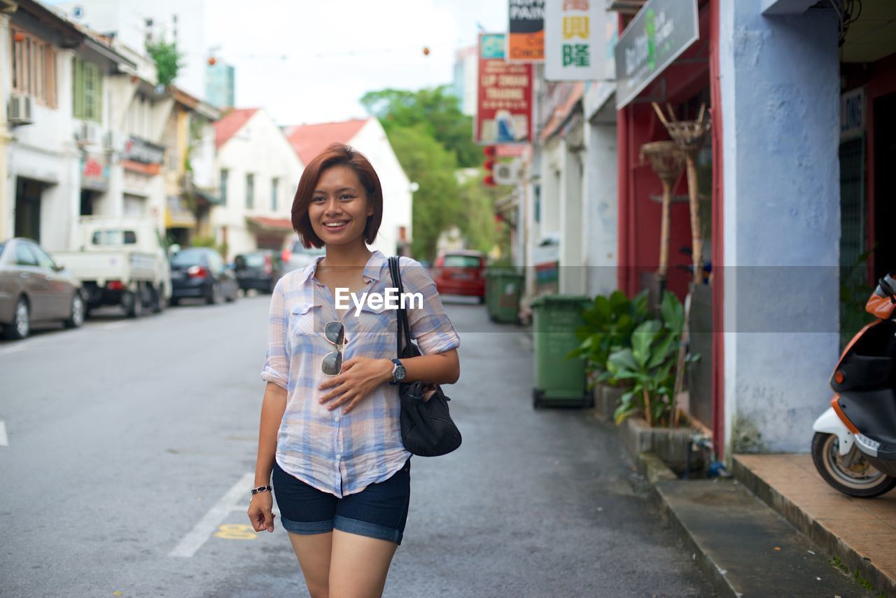 Smiling woman looking away while standing on street in city