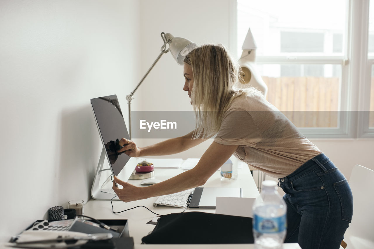 Side view of female graphic designer touching desktop monitor at home