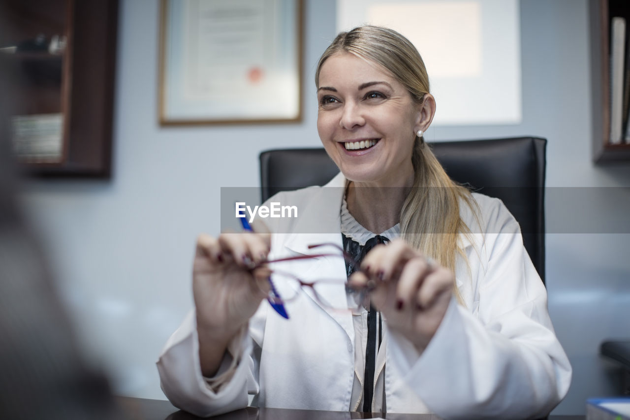 Female optometrist talking to patient, holding spectacles