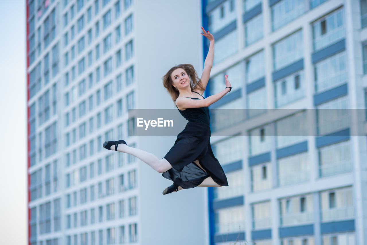 FULL LENGTH OF YOUNG WOMAN JUMPING AGAINST BUILDING