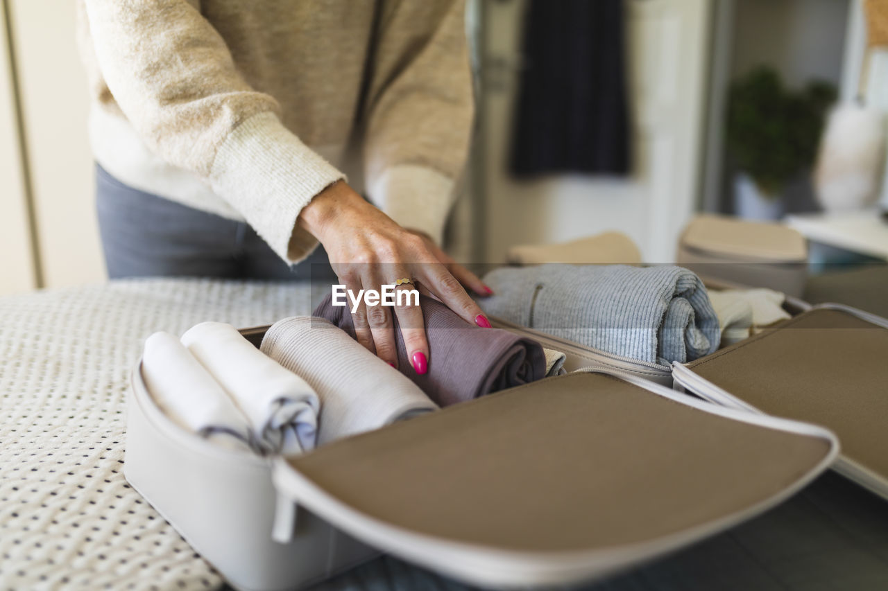 Hand of woman arranging rolled up cloths in bag on bed