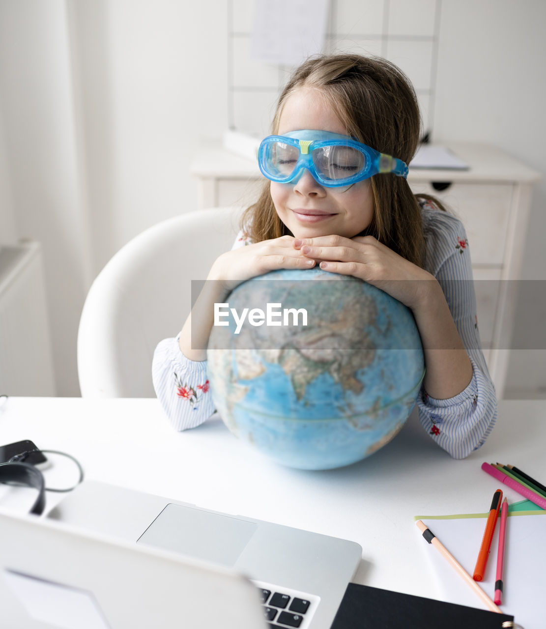 Cute girl with closed eyes and globe at desk