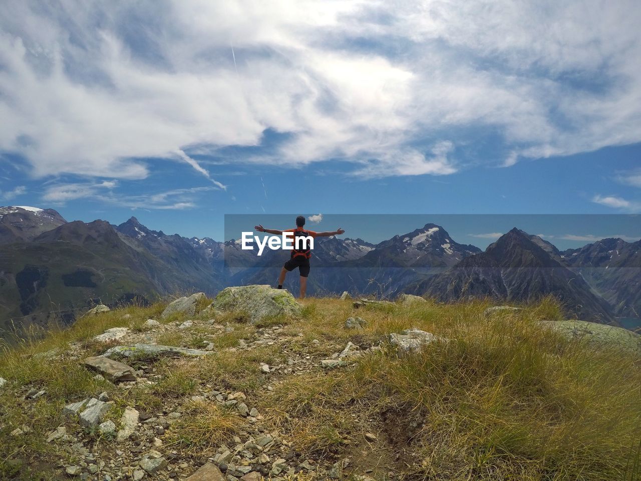 Rear view of young man with arms outstretched standing on mountain against cloudy sky
