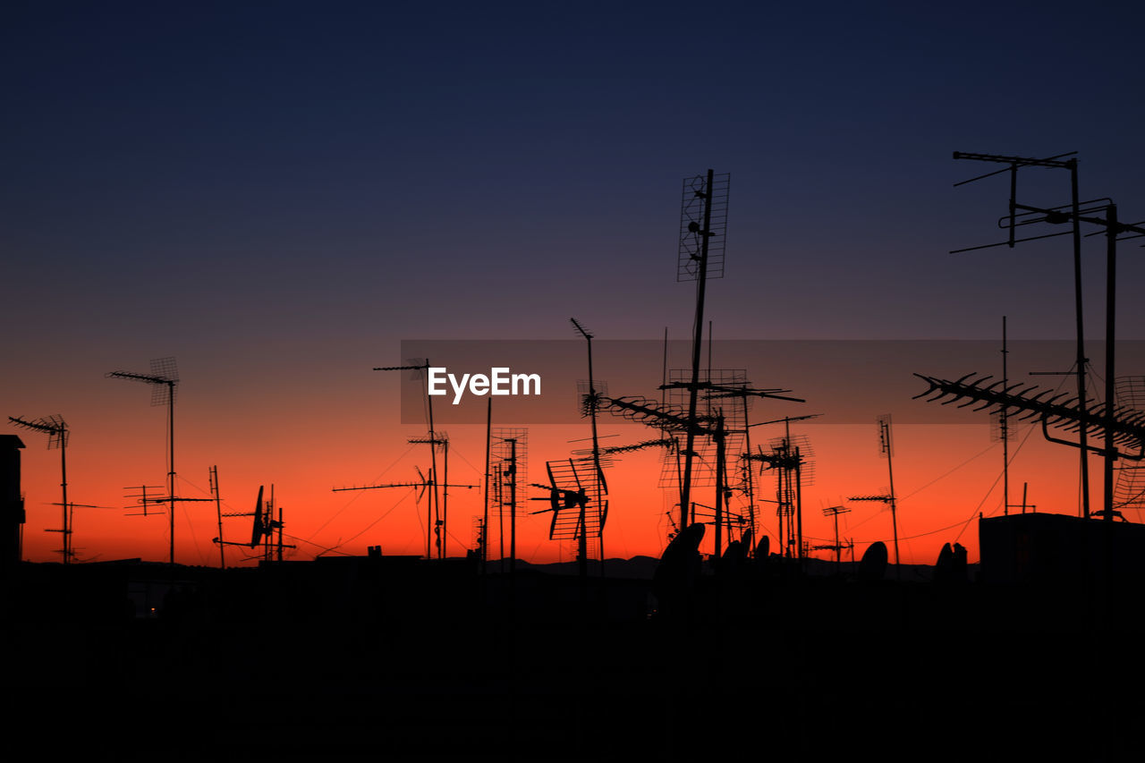 Silhouette antennas against clear sky at sunset