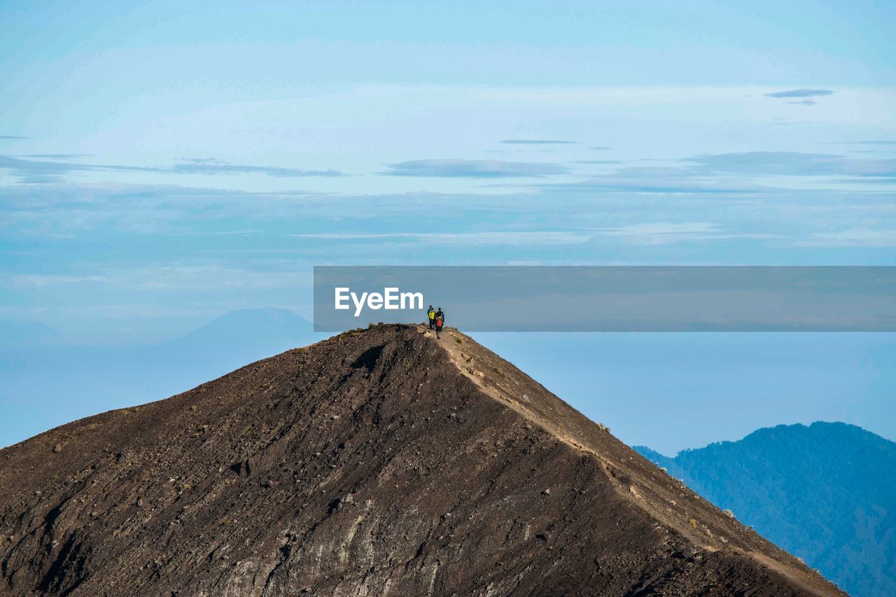 People hiking on top of mountain against cloudy sky