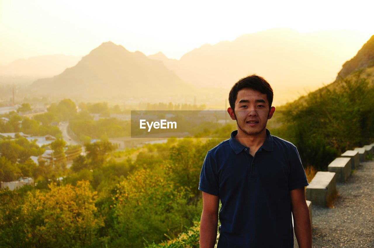 PORTRAIT OF YOUNG MAN STANDING ON LANDSCAPE