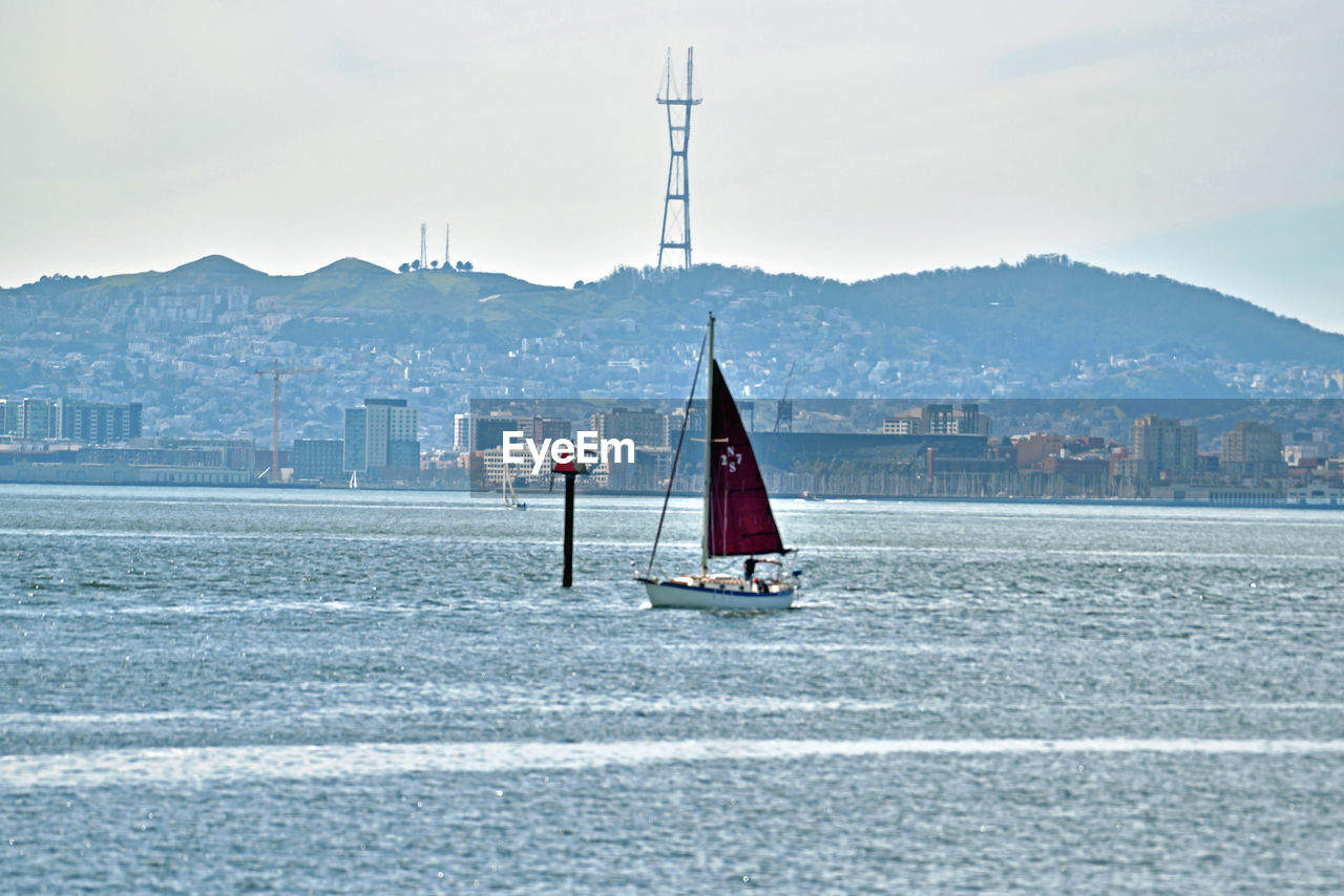 SAILBOAT ON SEA AGAINST BUILDINGS IN CITY