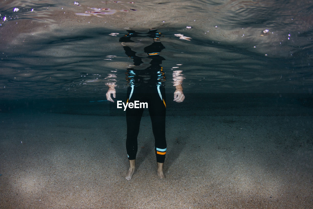 Underwater view of low section of man standing on sandy sea bottom