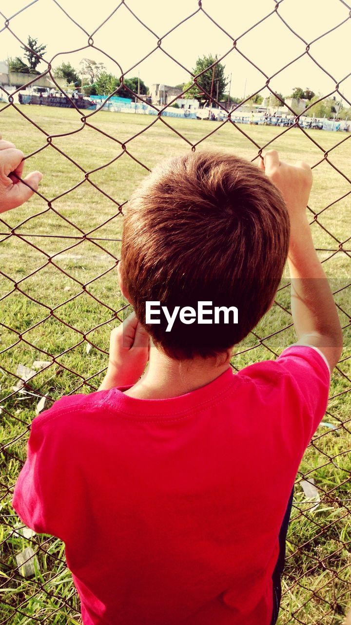 Rear view of boy looking at soccer field through fence