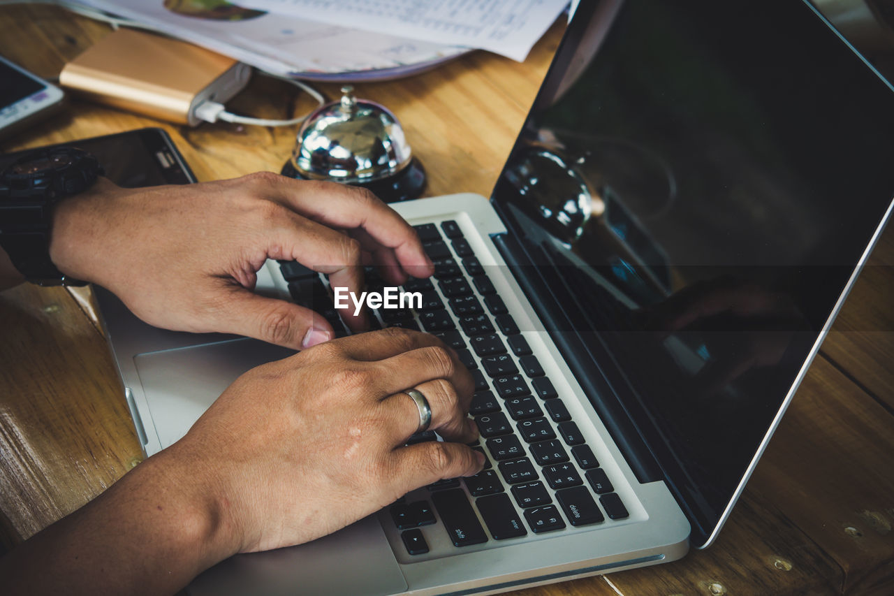 Cropped hands of man using laptop at table