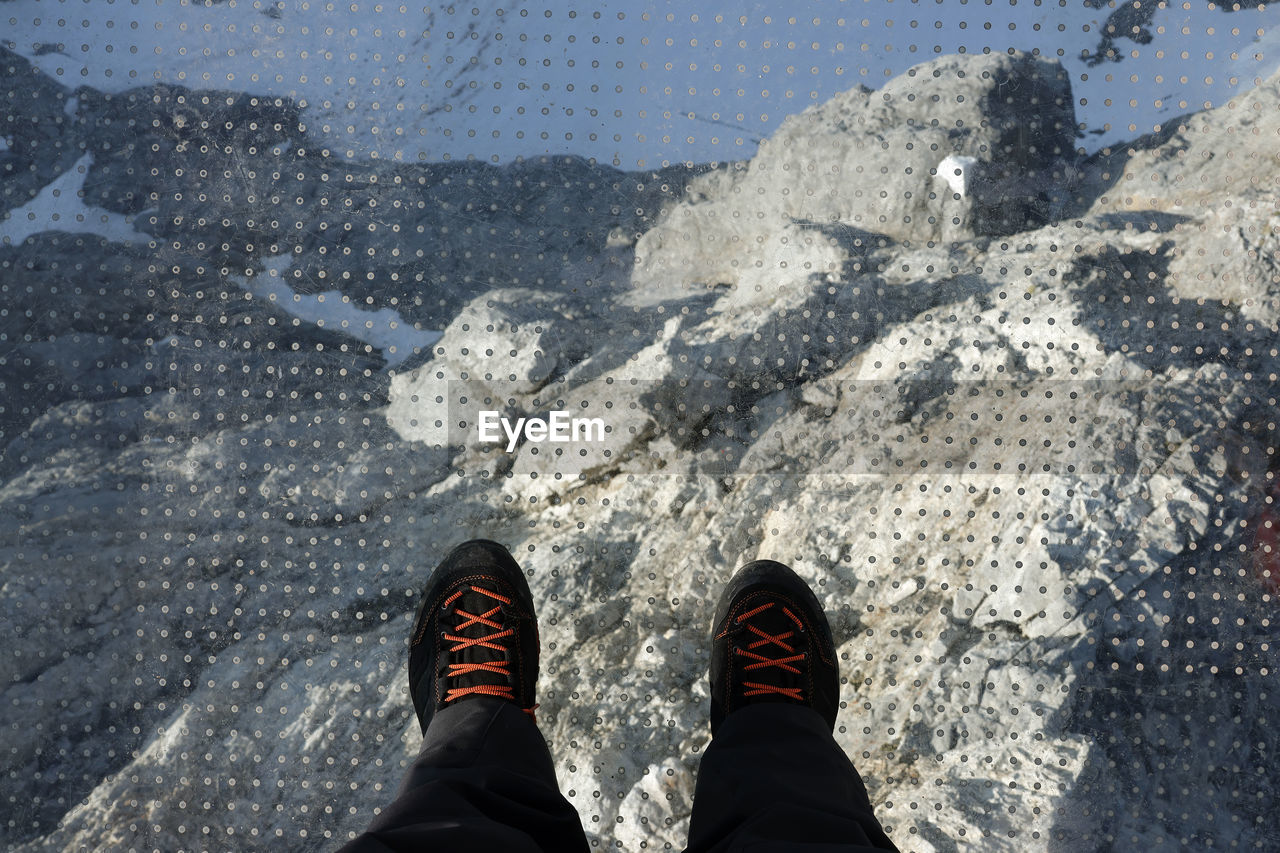 low section, human leg, shoe, personal perspective, one person, standing, lifestyles, nature, leisure activity, day, high angle view, men, snow, limb, outdoors, human limb, winter, land, blue, footwear, sunlight, shadow, human foot, water, rock, adult, clothing