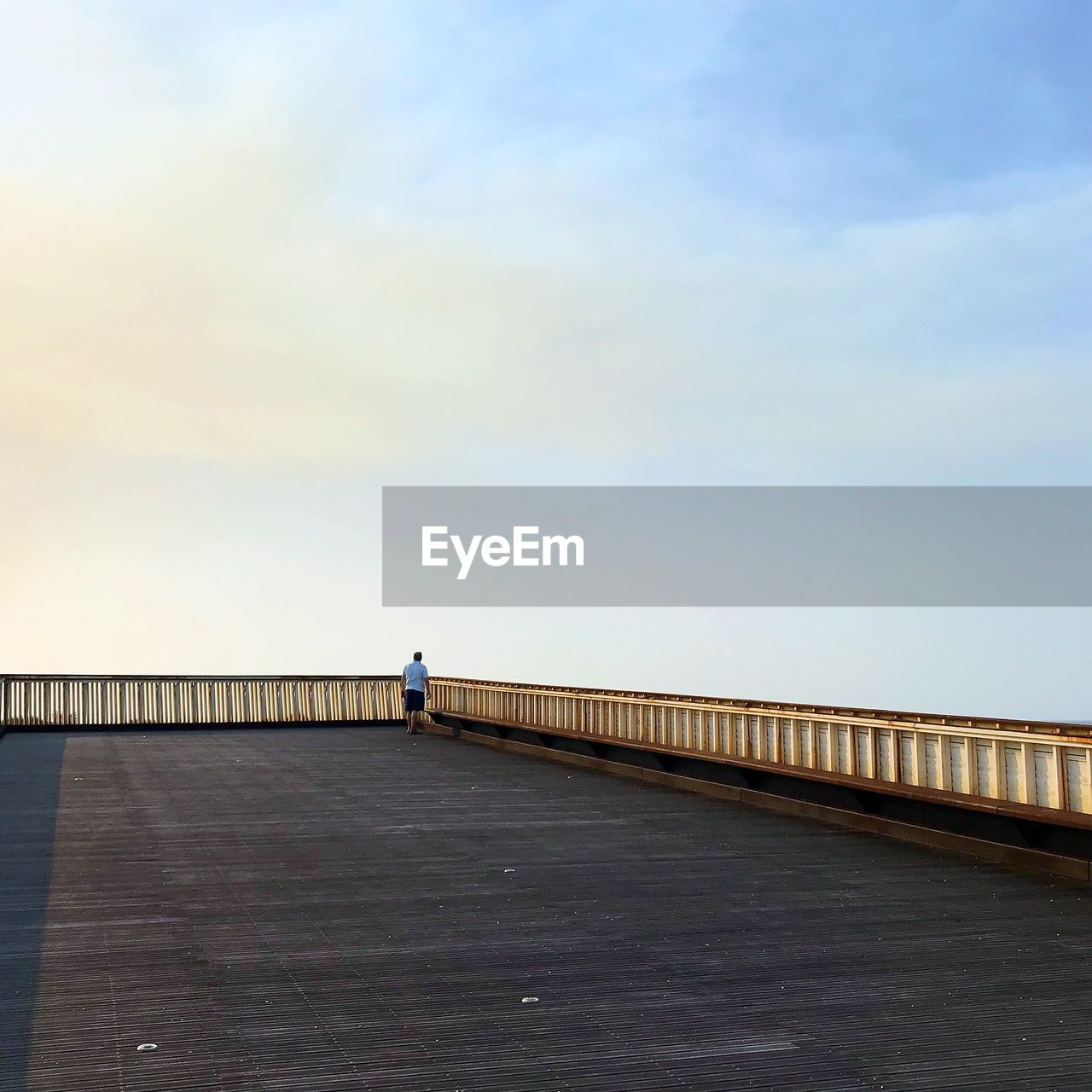 MAN STANDING ON FOOTBRIDGE OVER SEA AGAINST SKY