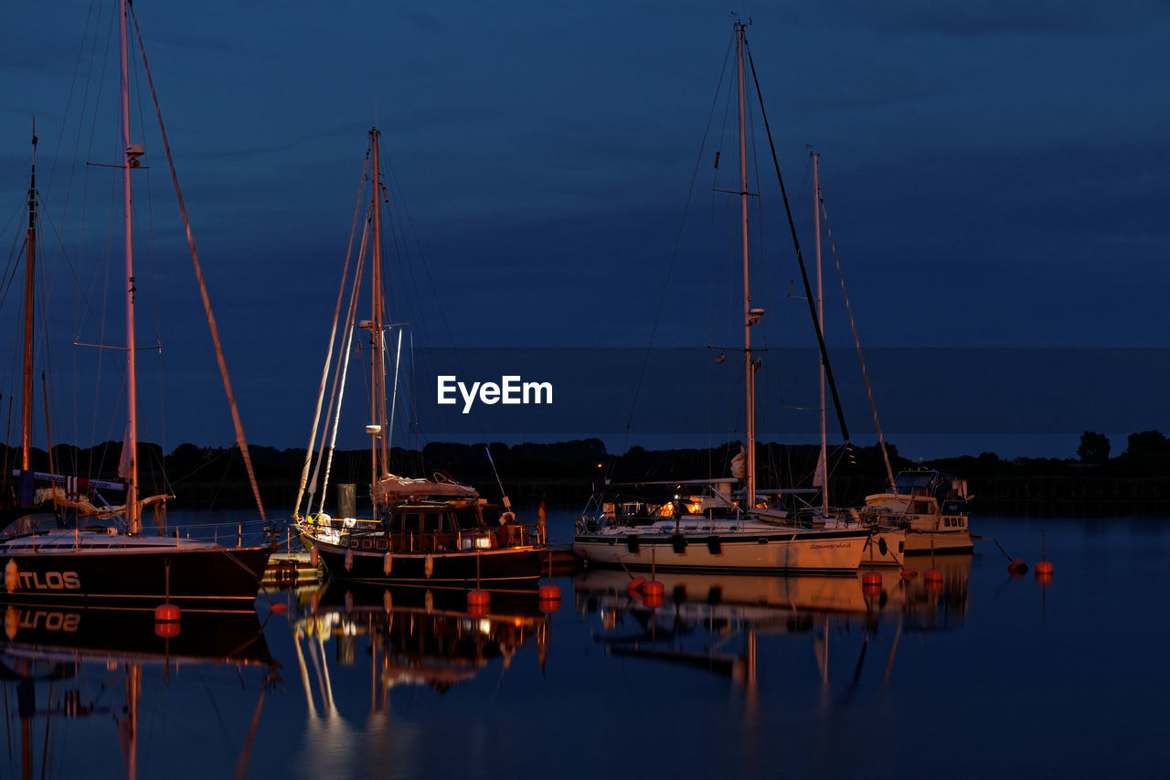 Sailboats moored in harbor at night