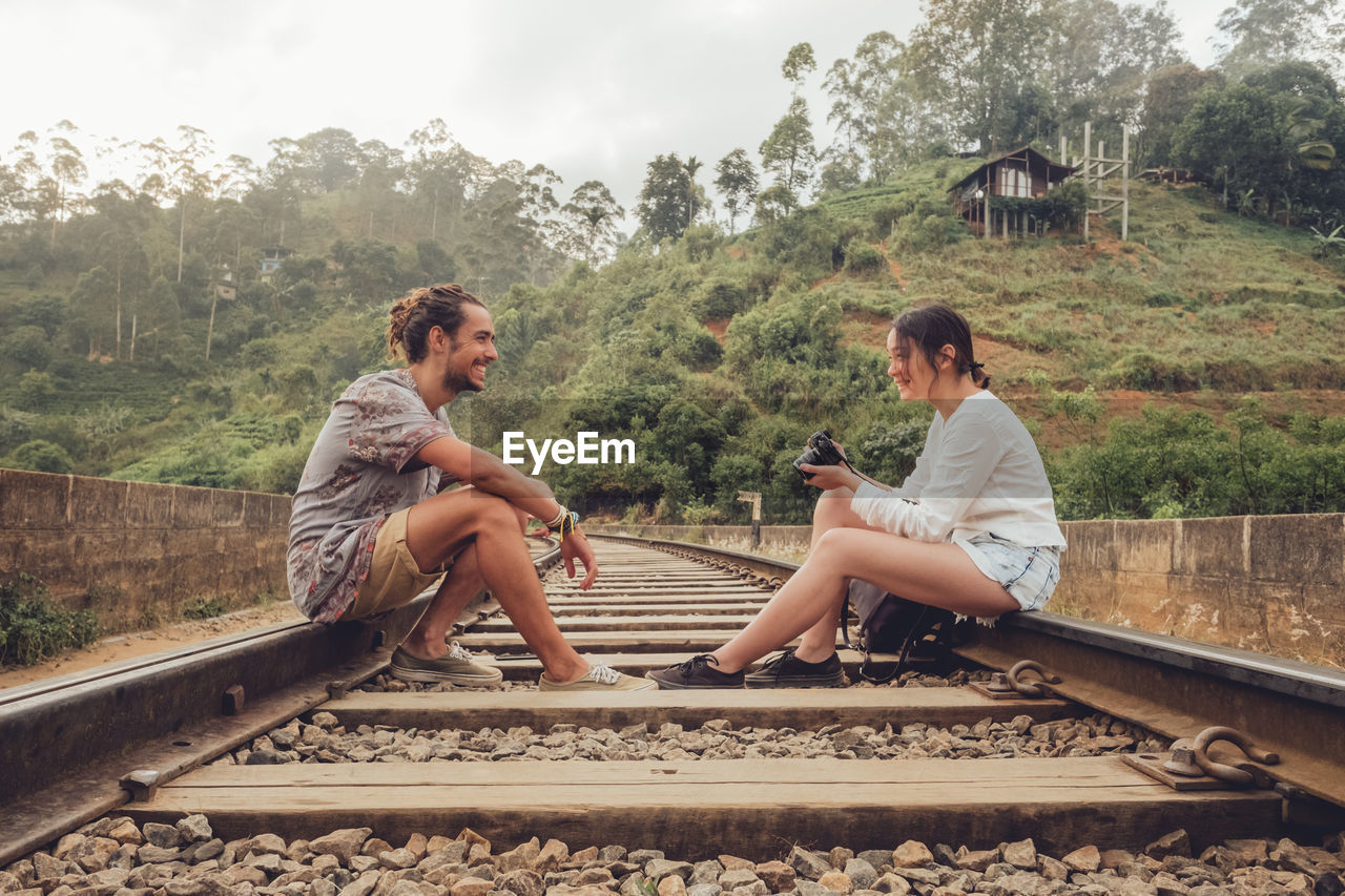 Woman shooting man with camera while sitting on railroad