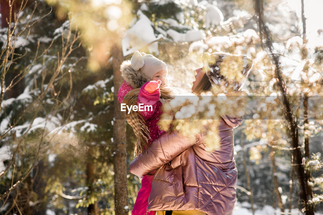 Mother playing with daughter in forest during winter