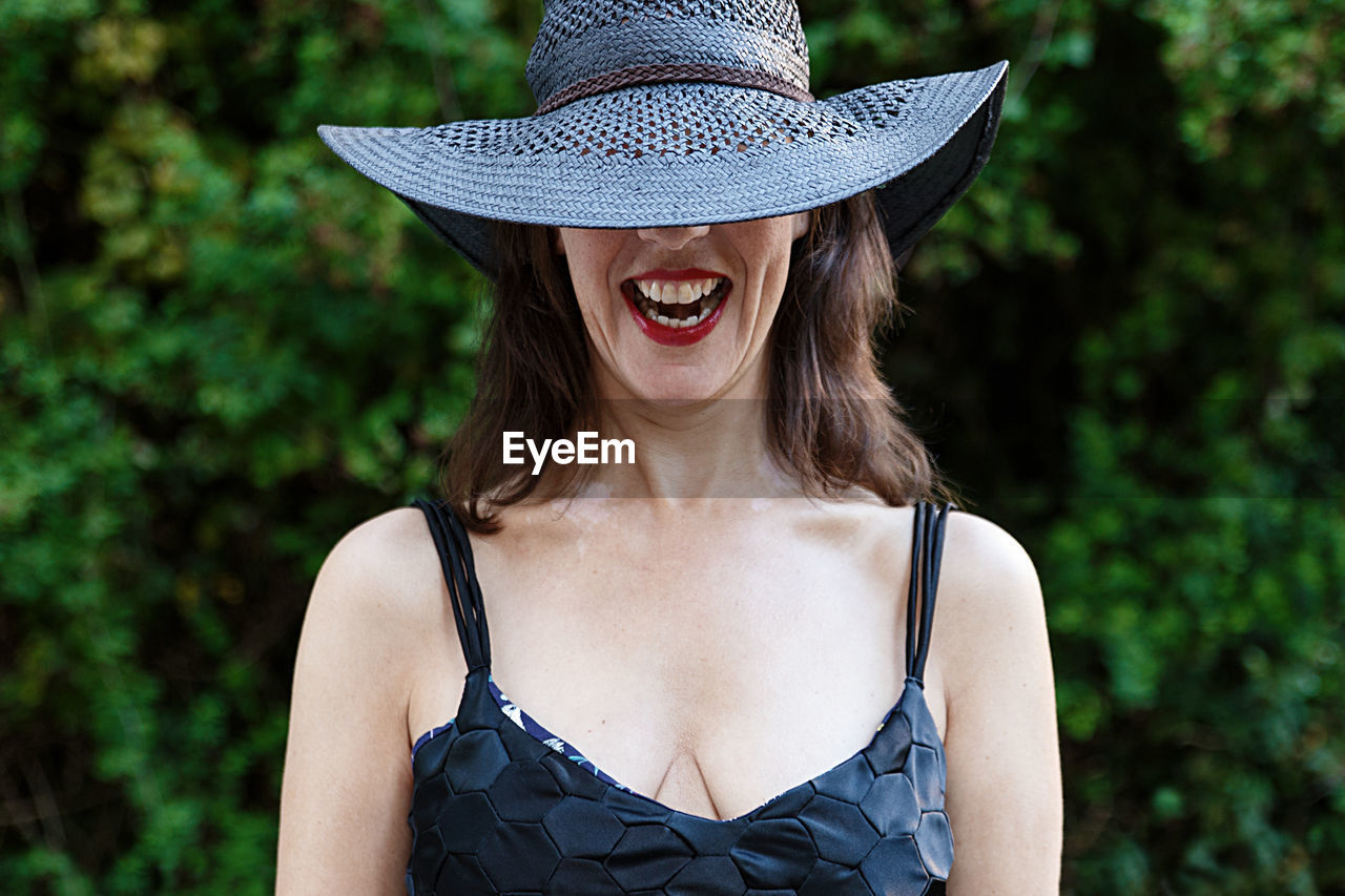 Smiling woman wearing hat standing against plants