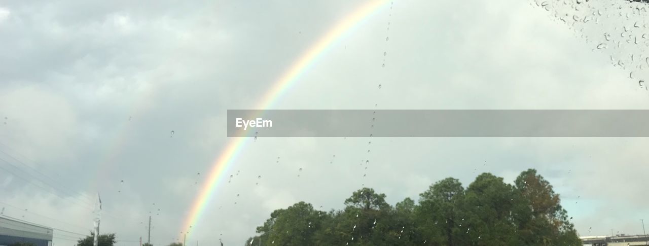 LOW ANGLE VIEW OF RAINBOW AGAINST CLOUDY SKY