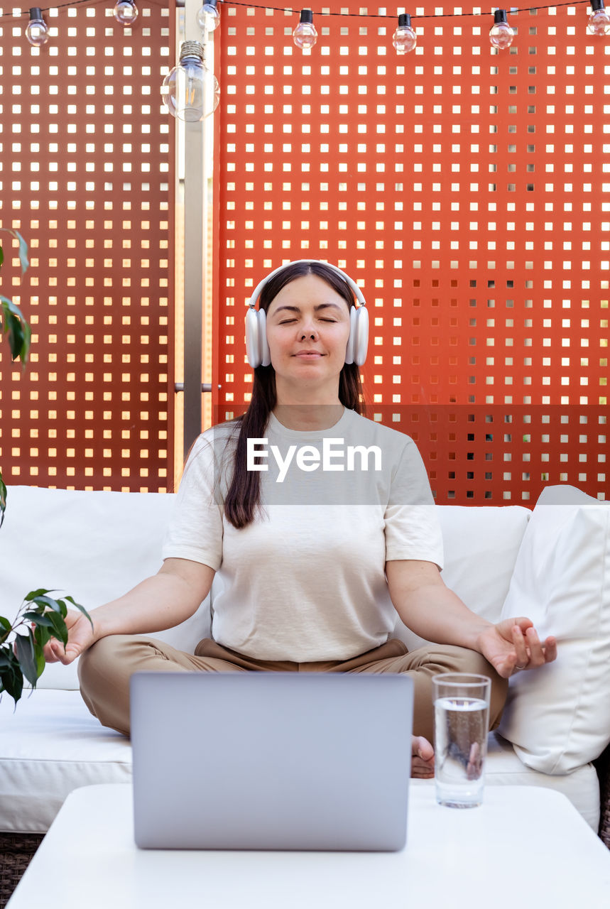 Woman having online meditation session with professional healer sitting with closed eyes on sofa 