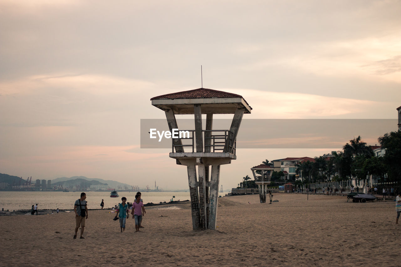 People by lookout tower at beach against sky