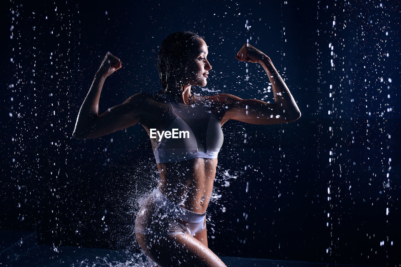 Woman exercising with dumbbell in water against black background
