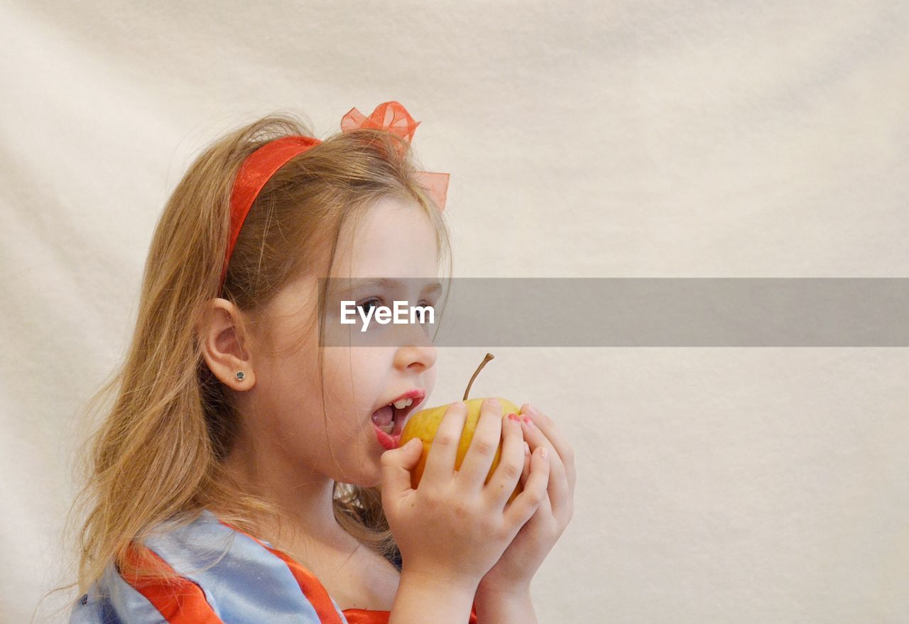 Close-up of cute girl eating apple against white fabric