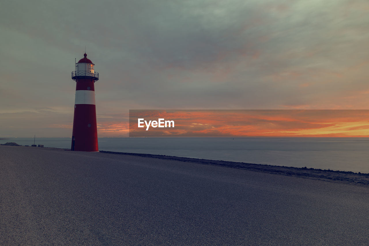 LIGHTHOUSE ON BEACH AGAINST SKY DURING SUNSET