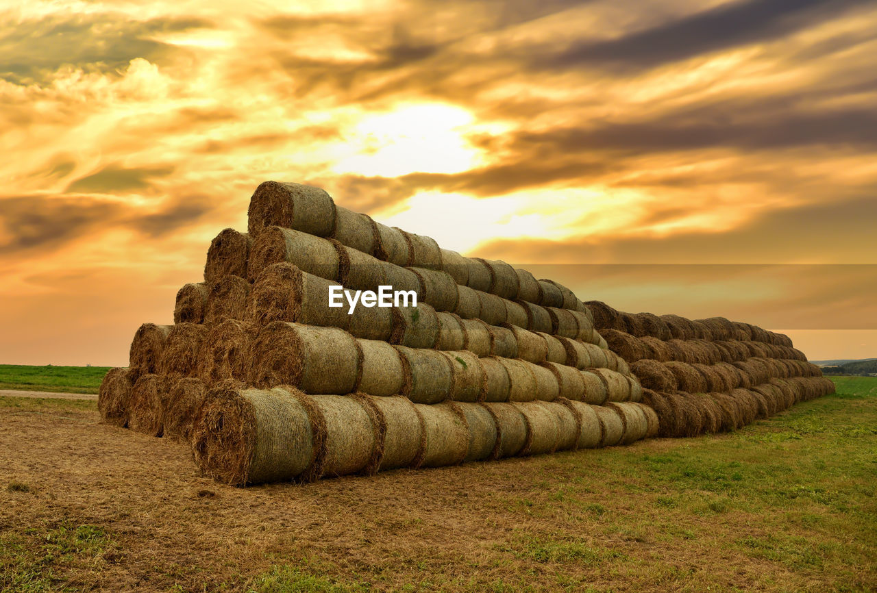 Stack of hay bales on field against sky during sunset