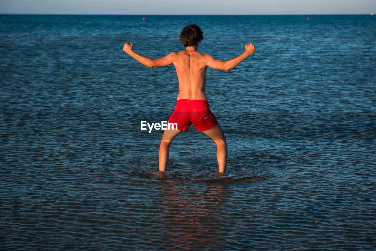 Rear view of shirtless man standing in sea