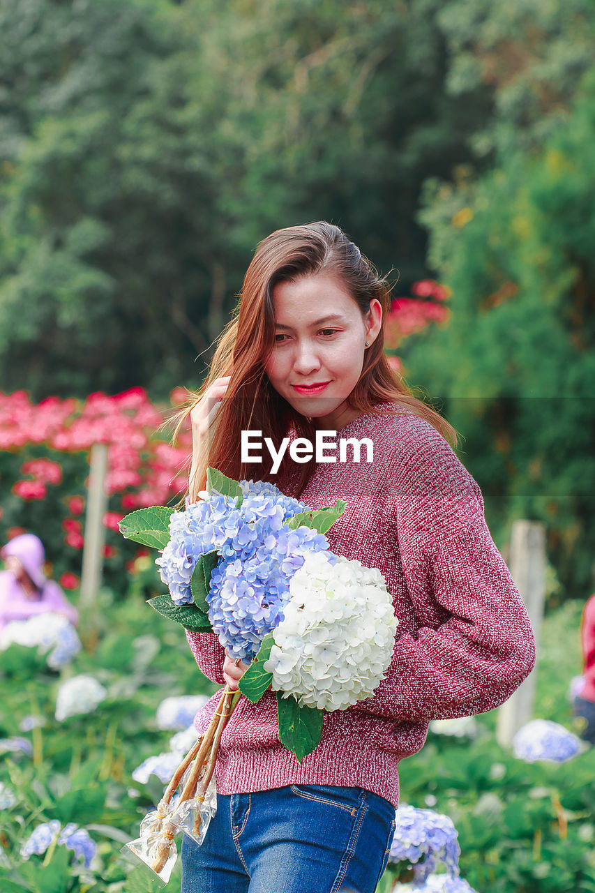 PORTRAIT OF A SMILING YOUNG WOMAN STANDING AGAINST PINK FLOWERS