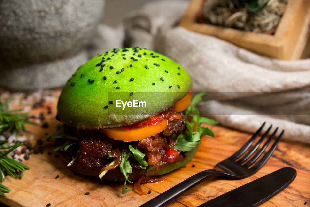 Green burger. green bun, with caramelized onions, slice of orange tomato, with arugula leaves.