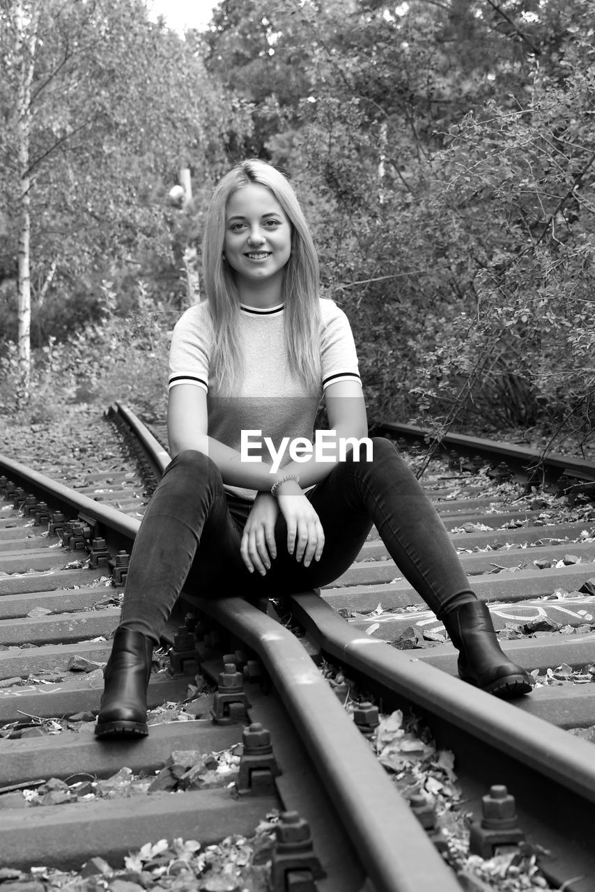 Portrait of young woman sitting on railroad track