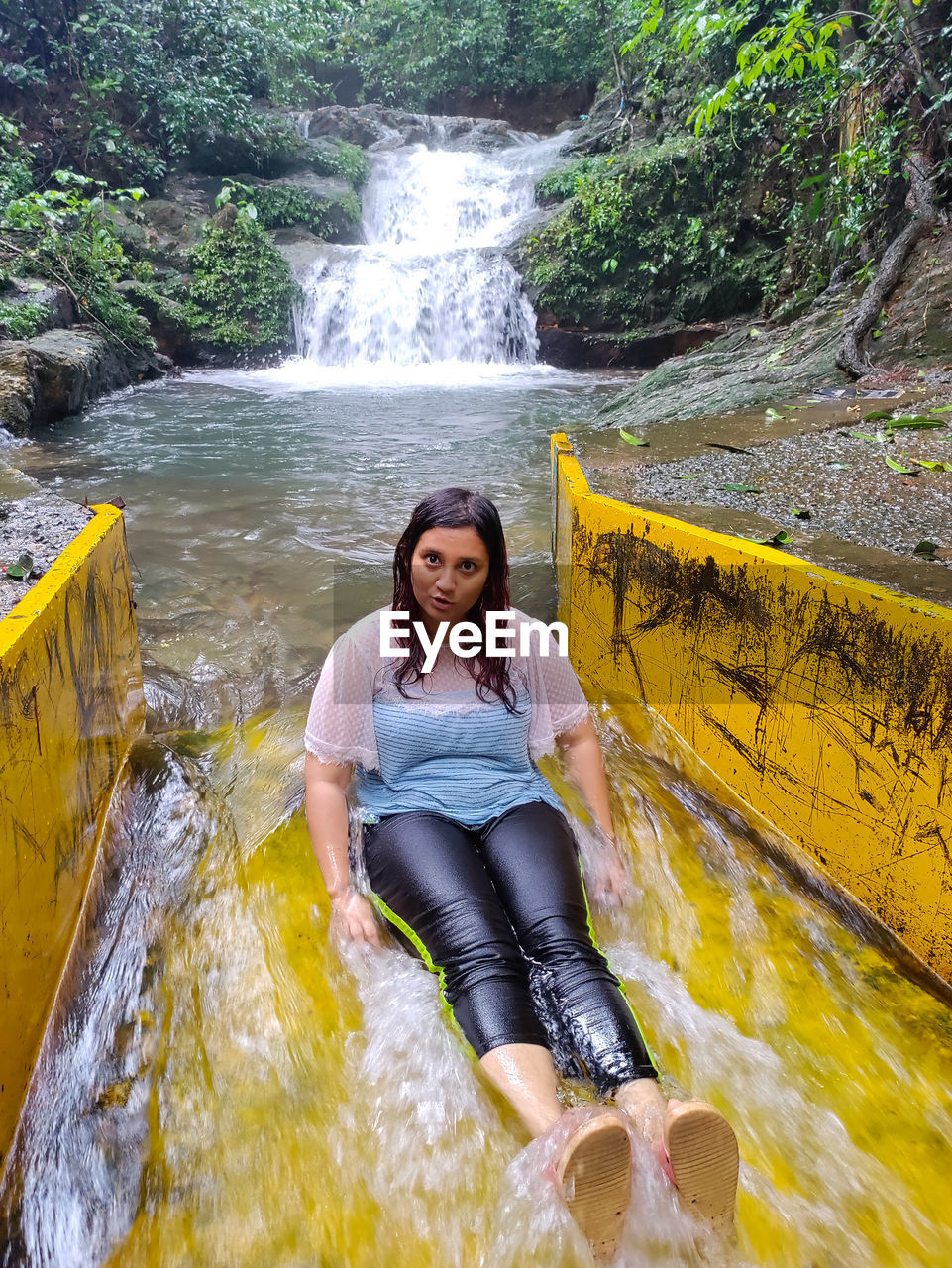 Portrait of young woman standing against waterfall