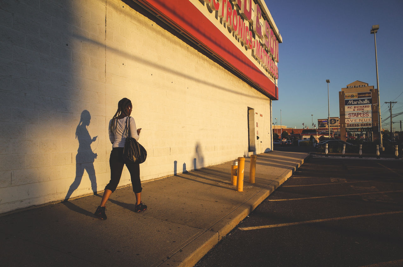 Rear view of woman walking on footpath in city against sky during sunset