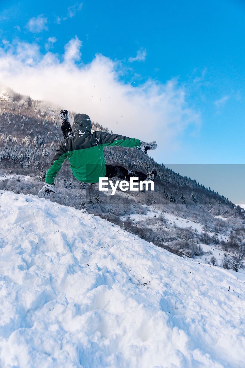 Rear view of person falling on snowcapped mountain against sky