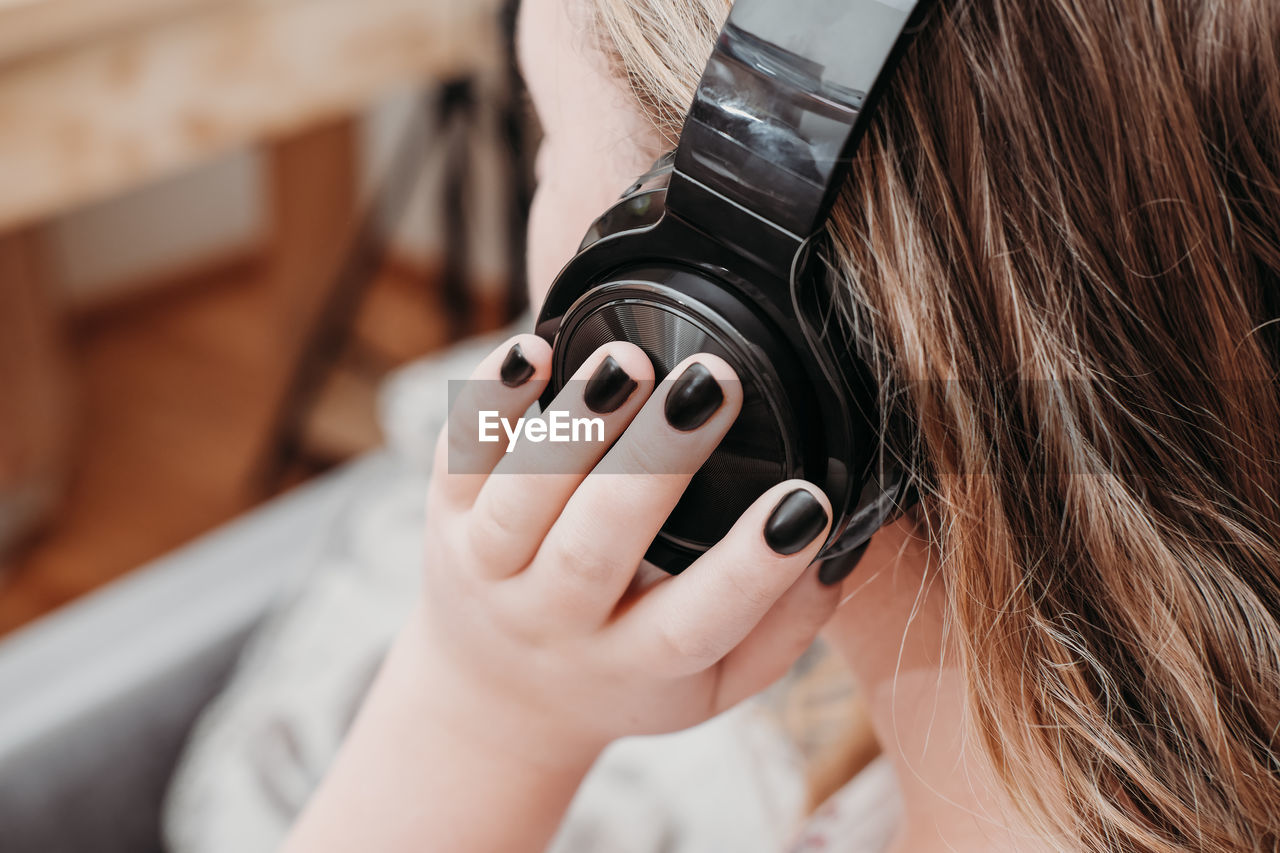 Caucasian teenager girl with black headphones enjoying music at home. unrecognizable person