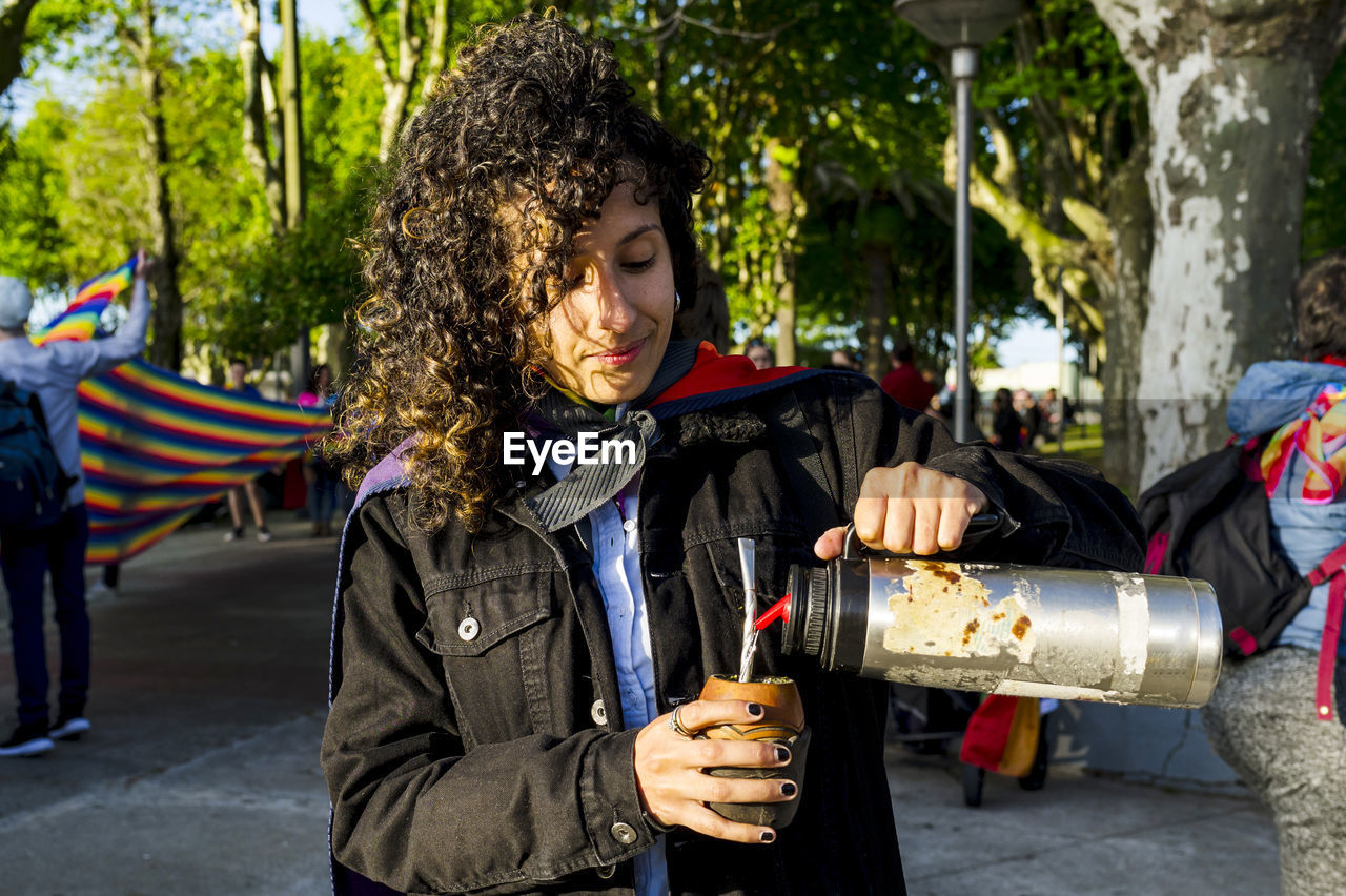 Woman drinking mate and holding a rainbow flag in an lgbtq pride march.