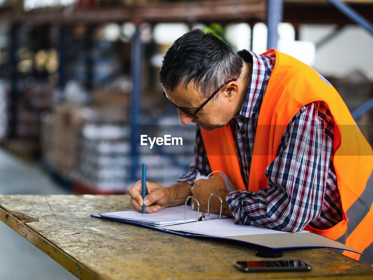Side view adult worker wearing uniform writing on clipboard while working in spacious storehouse