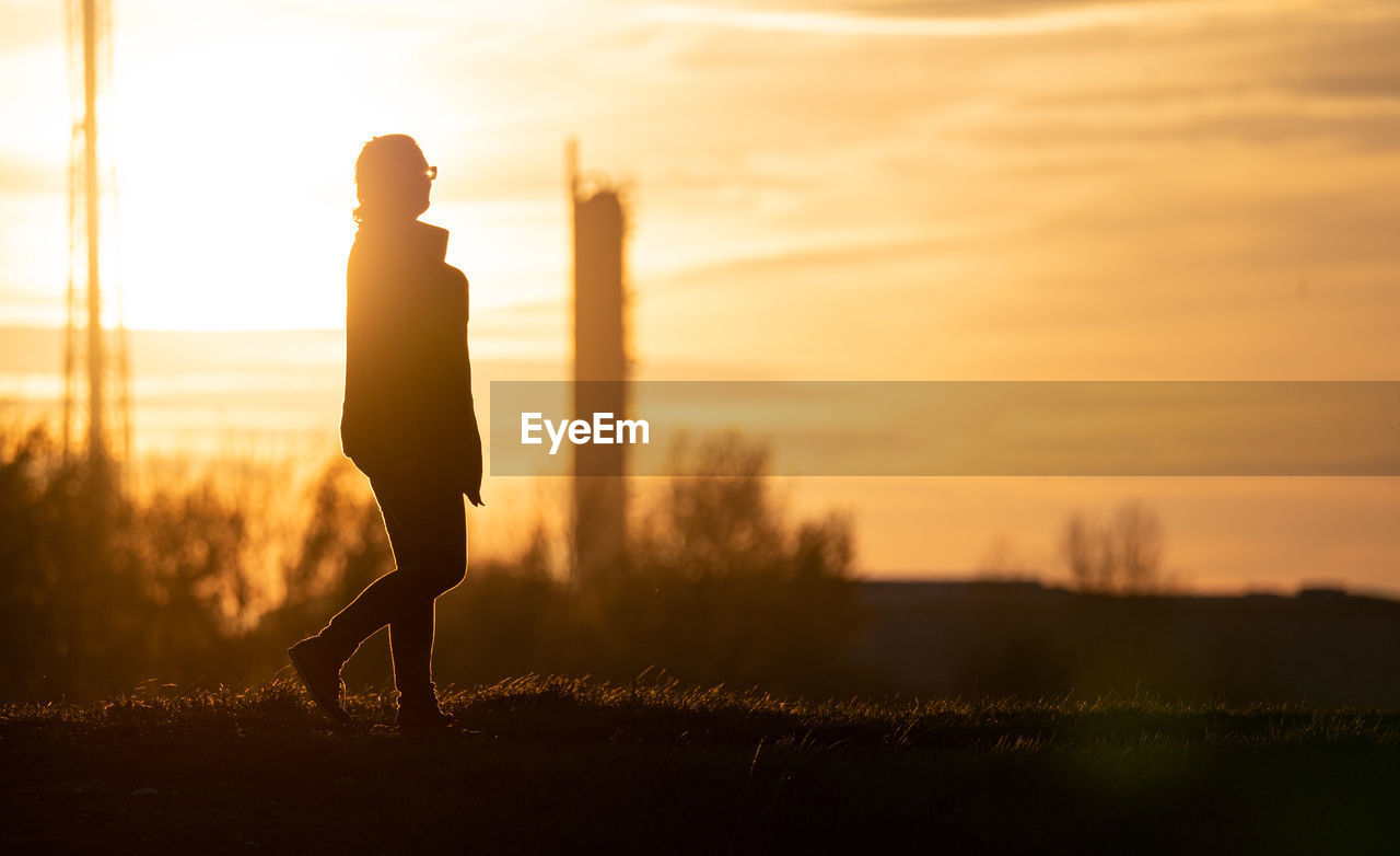 Silhouette woman standing on field against sky during sunset