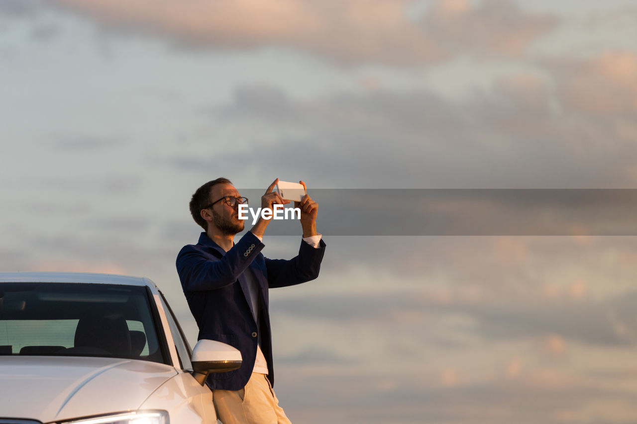 Man photographing while standing by car during sunset