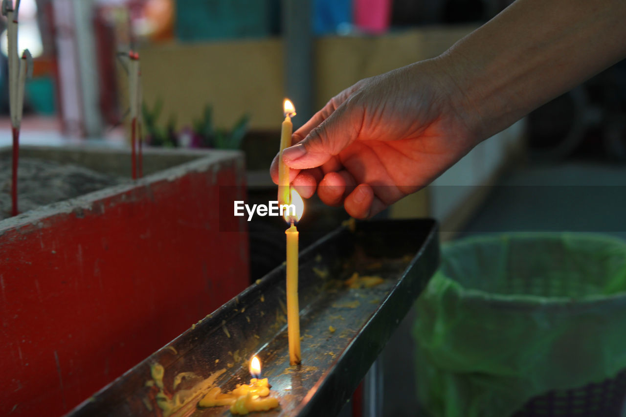 Close-up of hand holding lit candles in temple